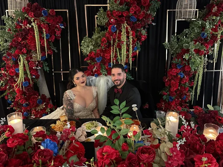 Bride and groom at sweetheart table with red and blue floral arch