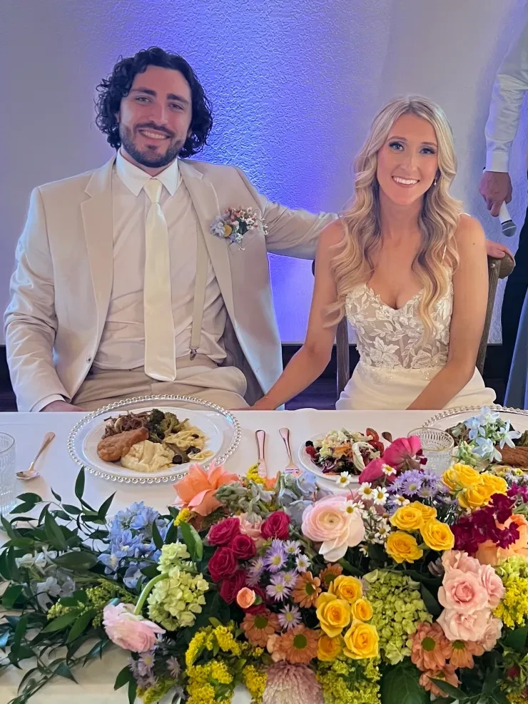 Couple at sweetheart table with vibrant colorful floral centerpiece and blue lighting
