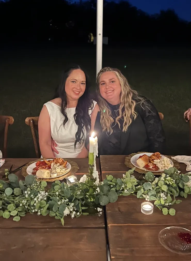 Two brides at candlelit outdoor dinner table with eucalyptus garland